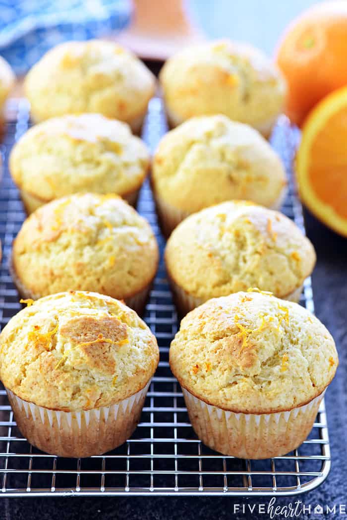 Orange Muffins ~ these lovely muffins are tender, and easy to make from scratch, with delicate flavors of vanilla and citrus from fresh orange juice and zest! | FiveHeartHome.com Orange Muffins on cooling rack with fresh oranges in background.