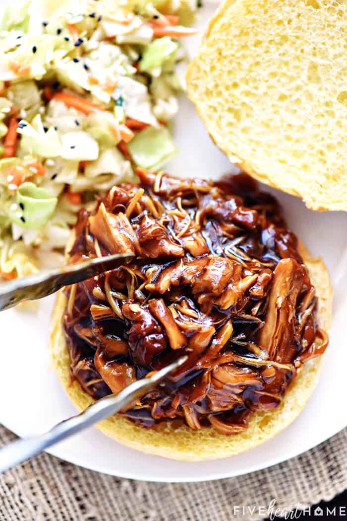 Shredded Teriyaki Chicken being put on a sandwich bun.