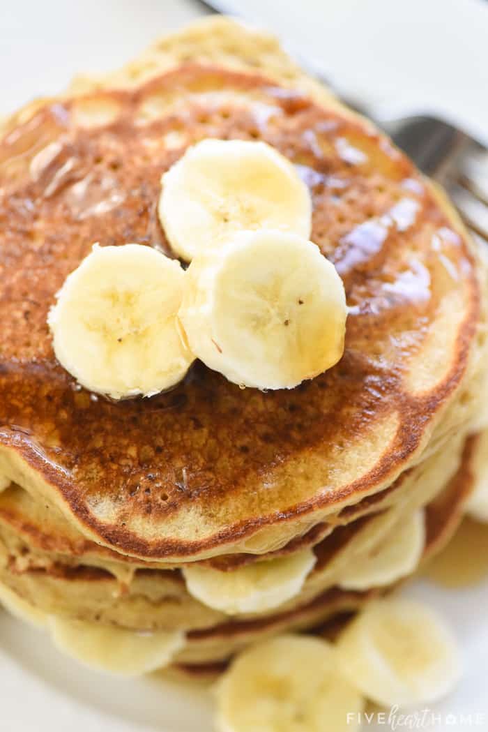 Banana Pancakes in a stack with syrup and bananas on top