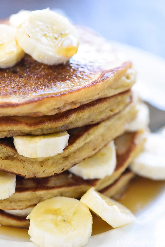 Zoomed in stack of Banana Pancakes with sliced bananas and maple syrup