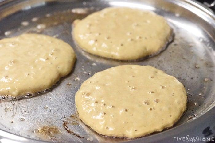Banana Pancakes cooking on a griddle on first side, with bubbles on top surface
