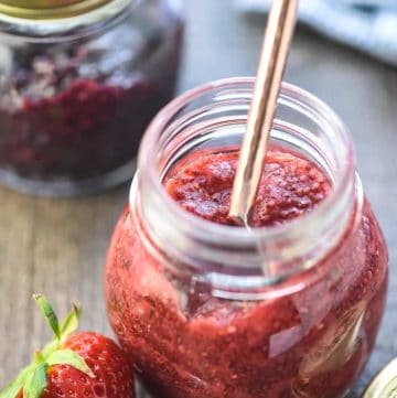 Chia Seed Jam in jars on table with spoon and strawberry.