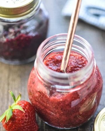 Chia Seed Jam in jars on table with spoon and strawberry.
