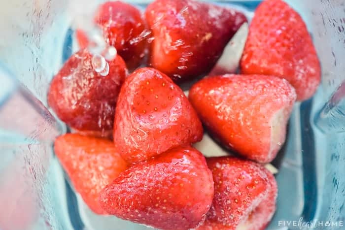 Rosé wine being poured over frozen strawberries in blender