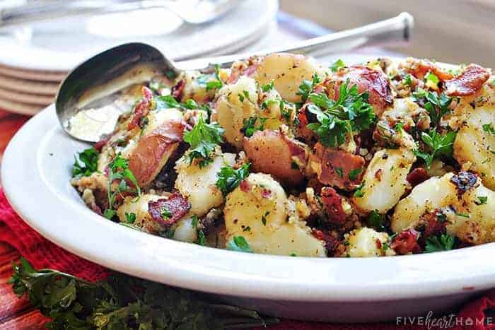 Warm German Potato Salad in white serving bowl with spoon.