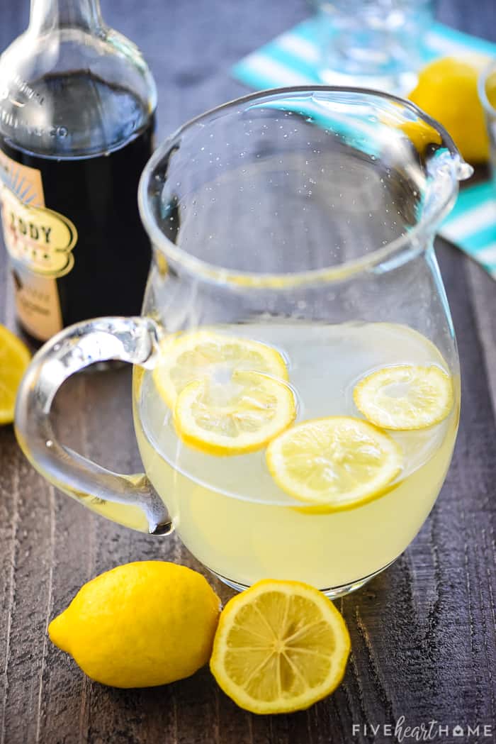 Glass pitcher of lemonade with lemon slices floating in it.