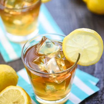 Two glasses of Boozy Arnold Palmer Drinks on napkins with lemons.