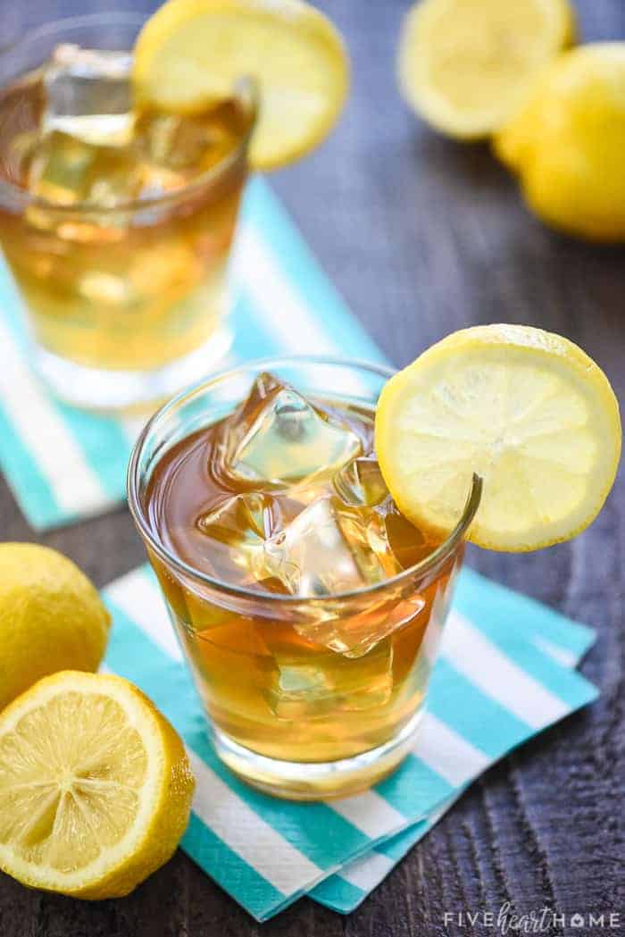 Two glasses of Boozy Arnold Palmer Drink on striped napkins with lemons.