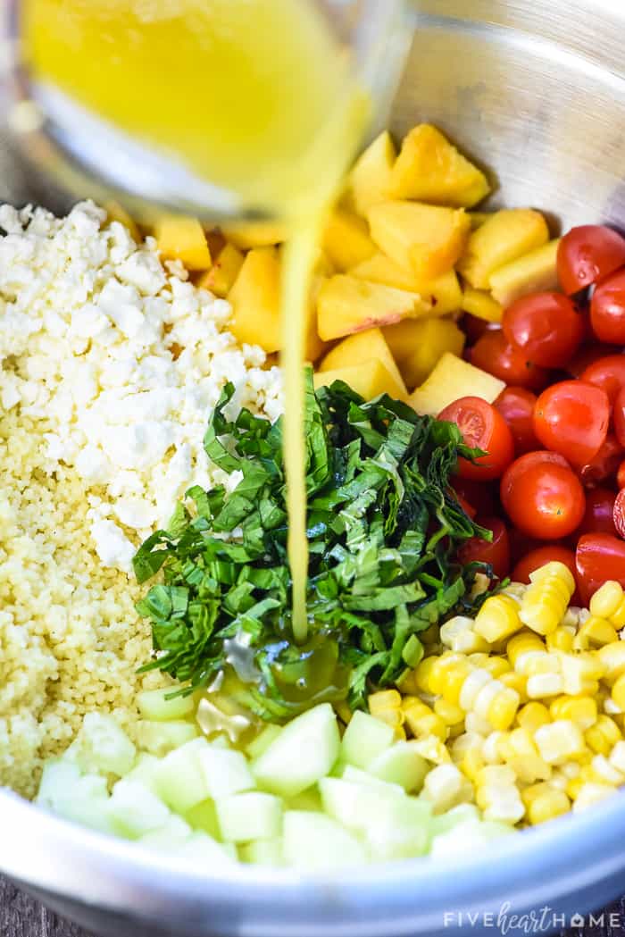 Honey lime dressing being poured over couscous, cucumbers, corn, tomatoes, peaches, feta, and basil