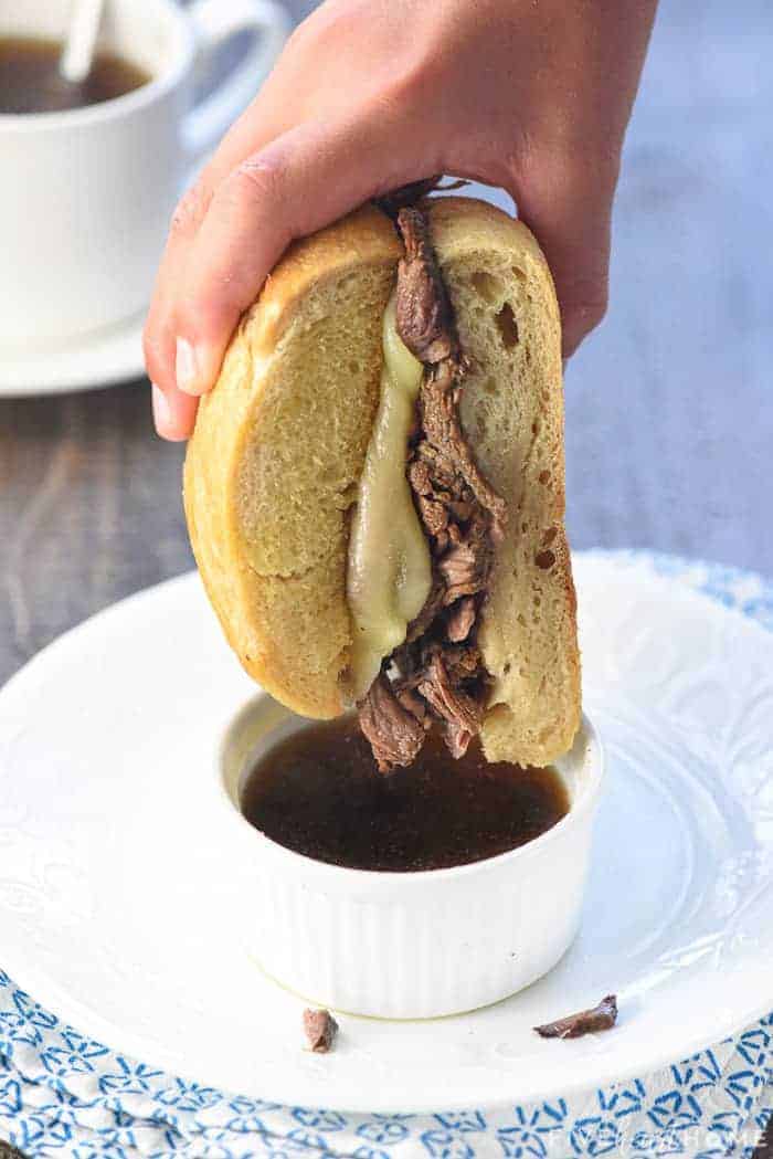 Slow Cooker French Dip sandwich being dipped into au jus.