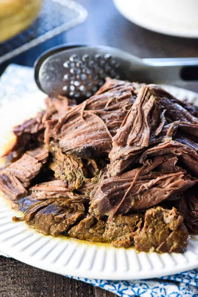 Pile of shredded beef on plate with tongs.