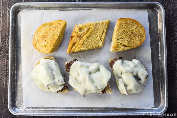 Slow Cooker French Dip sandwiches on baking sheet with melted cheese.