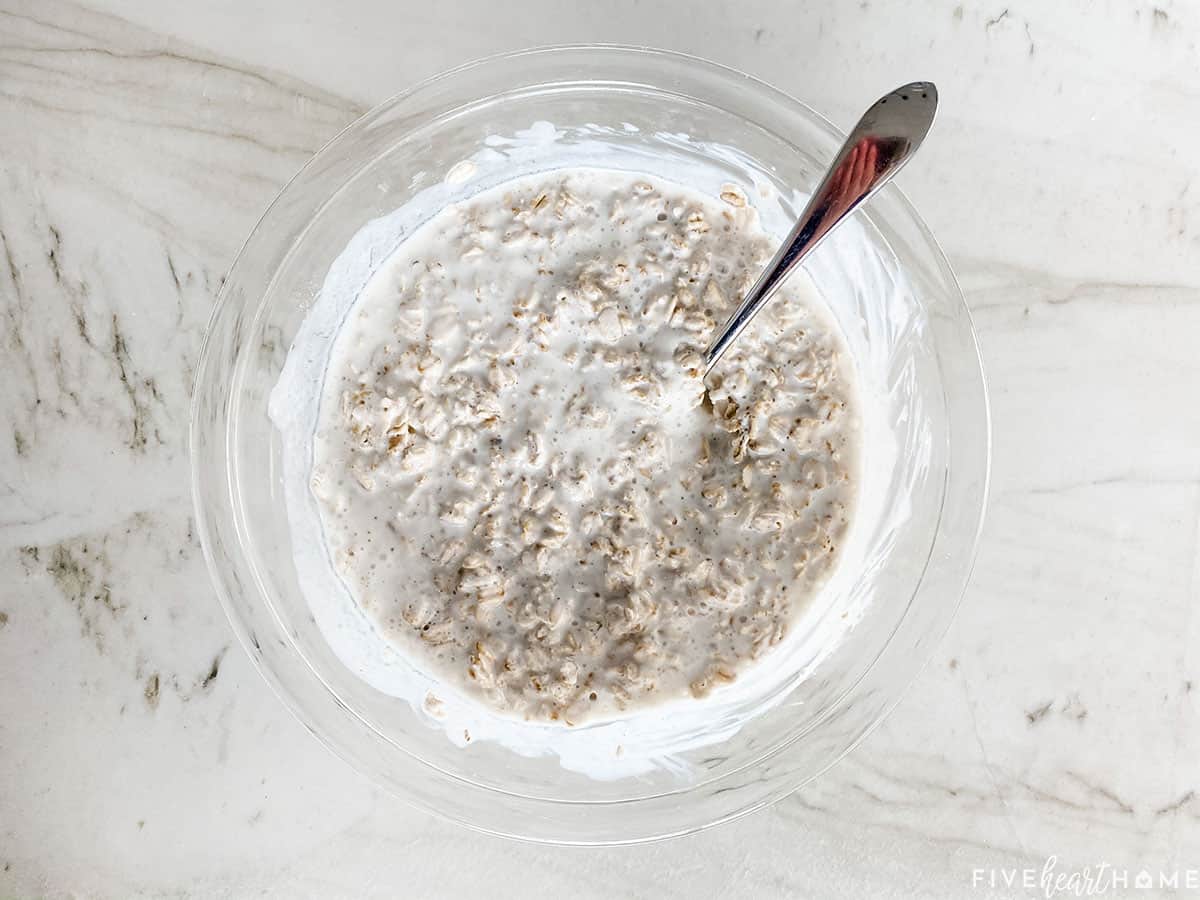 Aerial view of rolled oats stirred into buttermilk in a bowl.