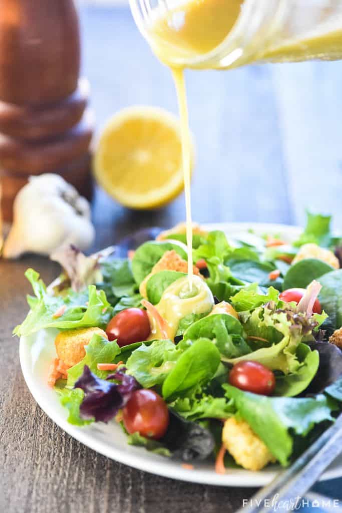 Pouring Champagne Vinaigrette recipe over a salad.