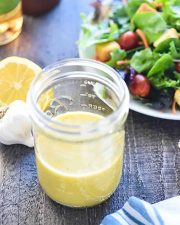 Jar of Champagne Vinaigrette on table with ingredients to make it and salad in background