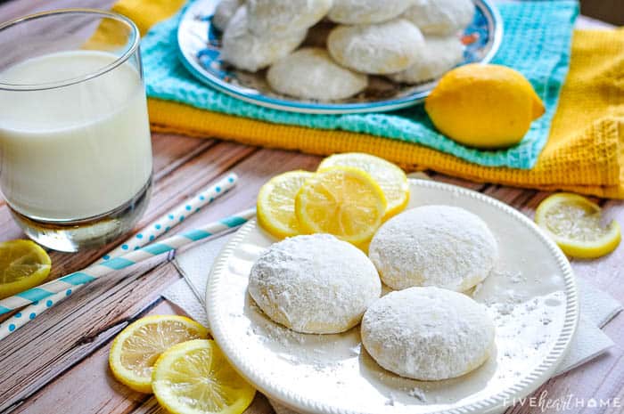 Lemon Cooler Cookies ~ soft, tender cookies bursting with fresh lemon and real butter, then coated in lemony powdered sugar! | FiveHeartHome.com Scene of cookies, milk, lemon slices, and colorful towels and straws.