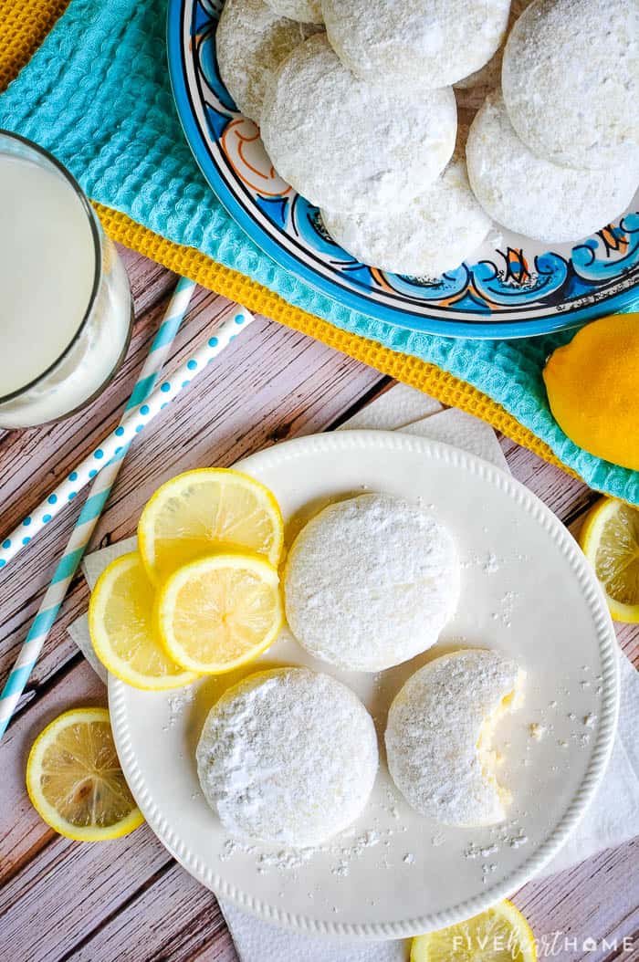 Lemon Cooler Cookies ~ soft, tender cookies bursting with fresh lemon and real butter, then coated in lemony powdered sugar! | FiveHeartHome.com Aerial view of Lemon Cooler Cookies on plates with lemon slices.