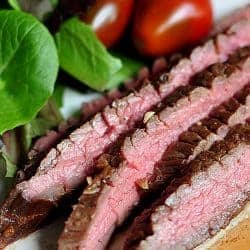 Close-up of medium-rare slices of grilled flank steak on a plate with sides