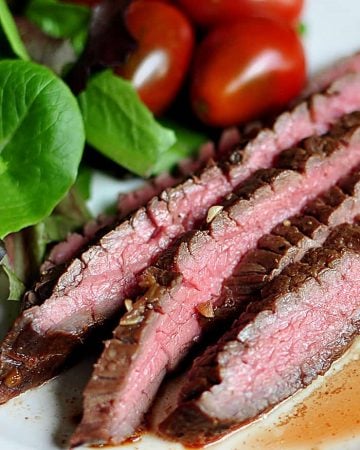 Close-up of medium-rare slices of grilled flank steak on a plate with sides