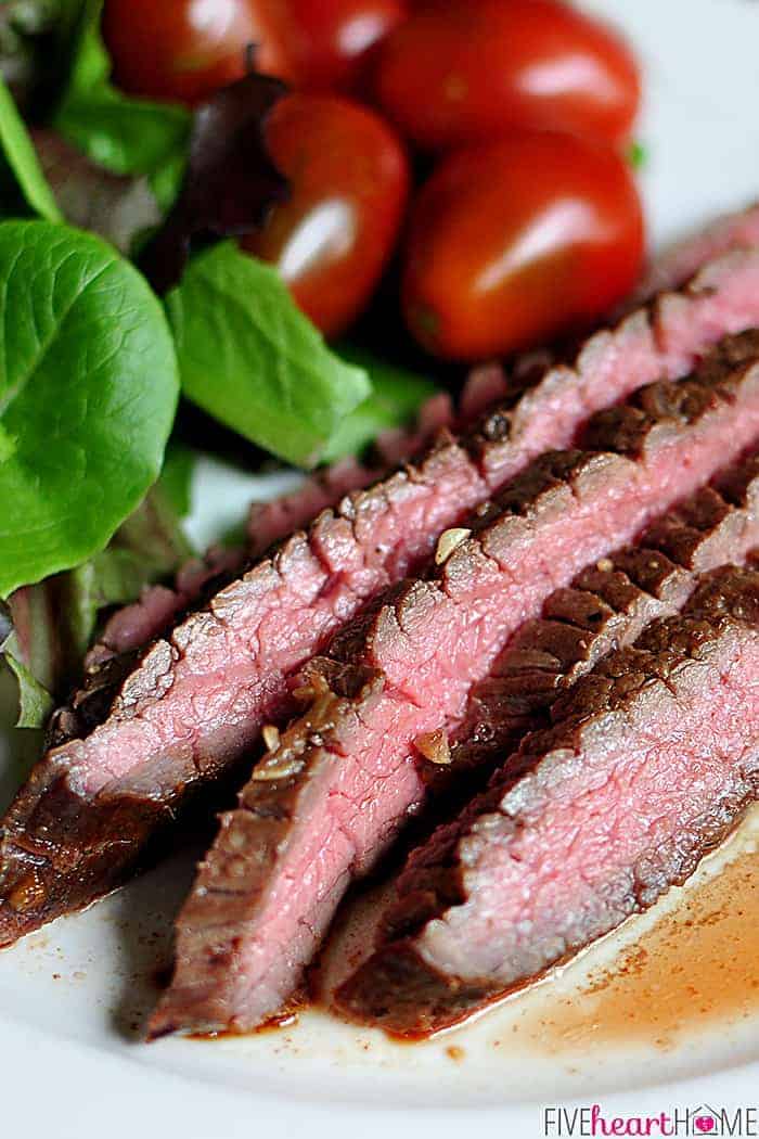 Close-up of medium-rare slices of grilled flank steak on a plate with sides