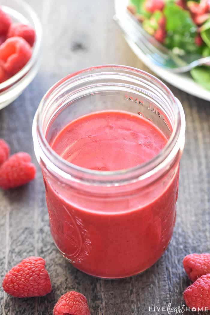 Jar of Raspberry Vinaigrette with salad and raspberries on table.