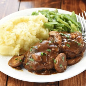 Hamburger Steaks with Mushroom Gravy on dinner plate with mashed potatoes and green beans.