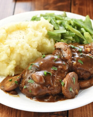 Hamburger Steaks with Mushroom Gravy on dinner plate with mashed potatoes and green beans.