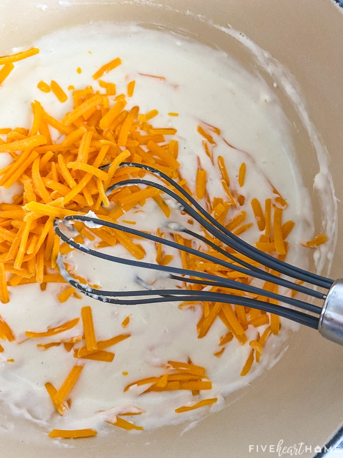 Shredded cheddar going into cheese sauce.