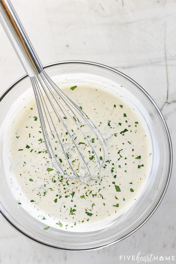 Aerial view of Ranch recipe in bowl with whisk, garnished with parsley.