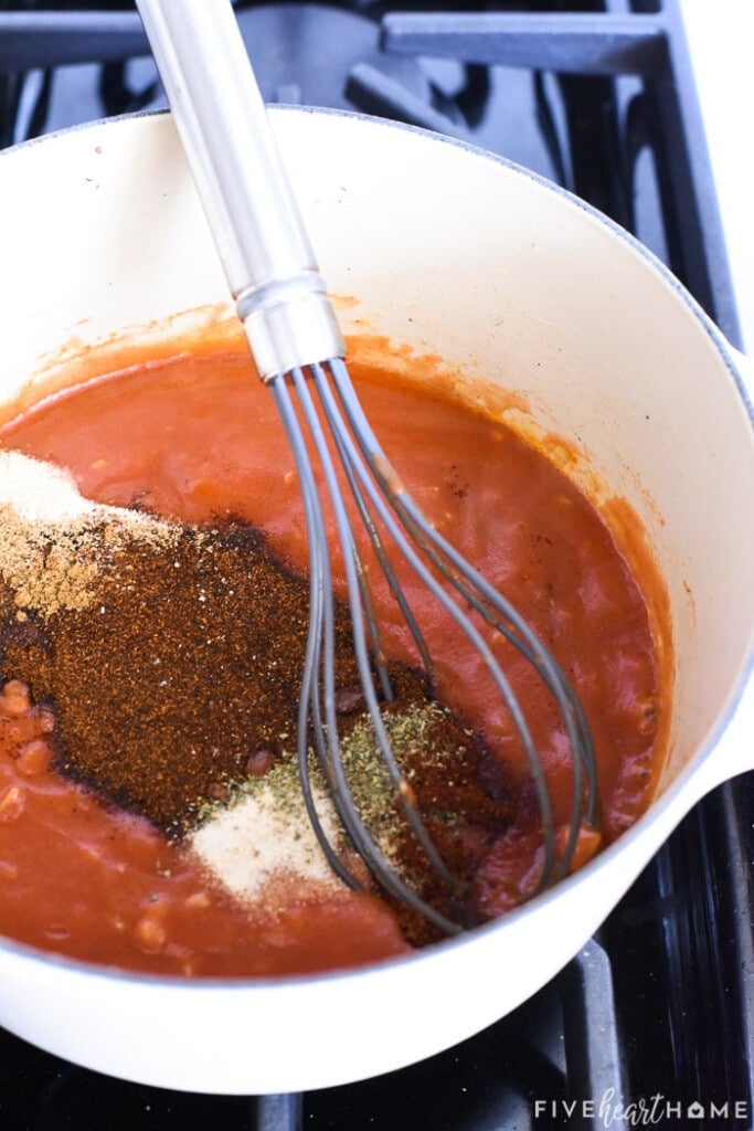 Sauce in pot with spices being whisked in.