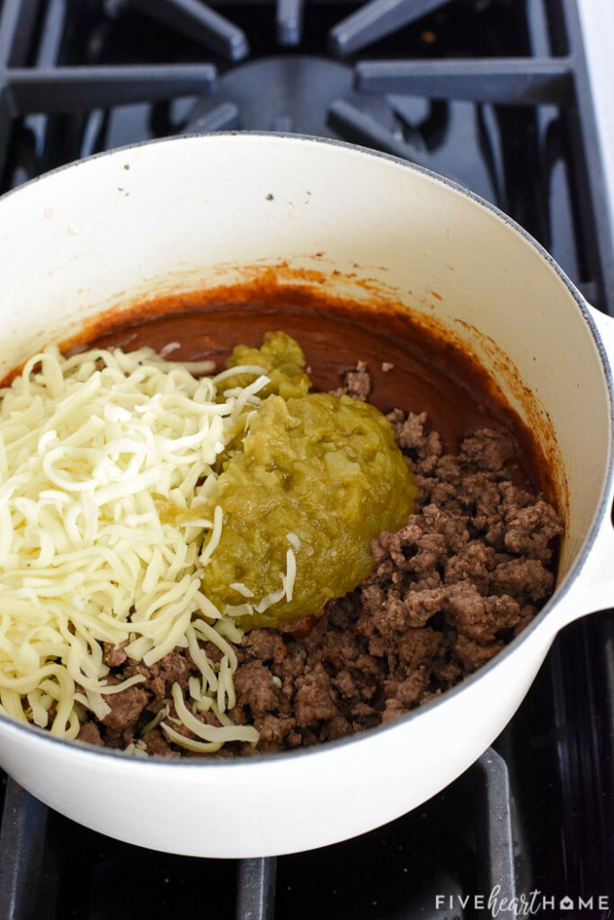 Ground beef, shredded cheese, and green chiles added to sauce in pot.