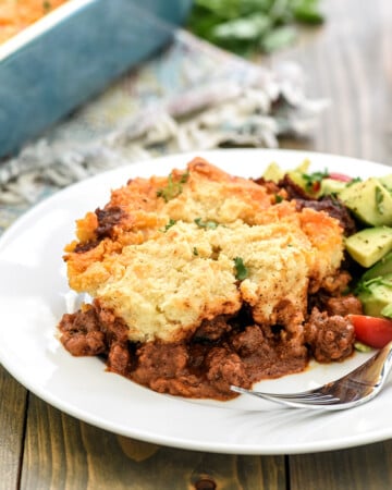 Tamale Pie recipe served on a plate with avocado tomato salad on the side.