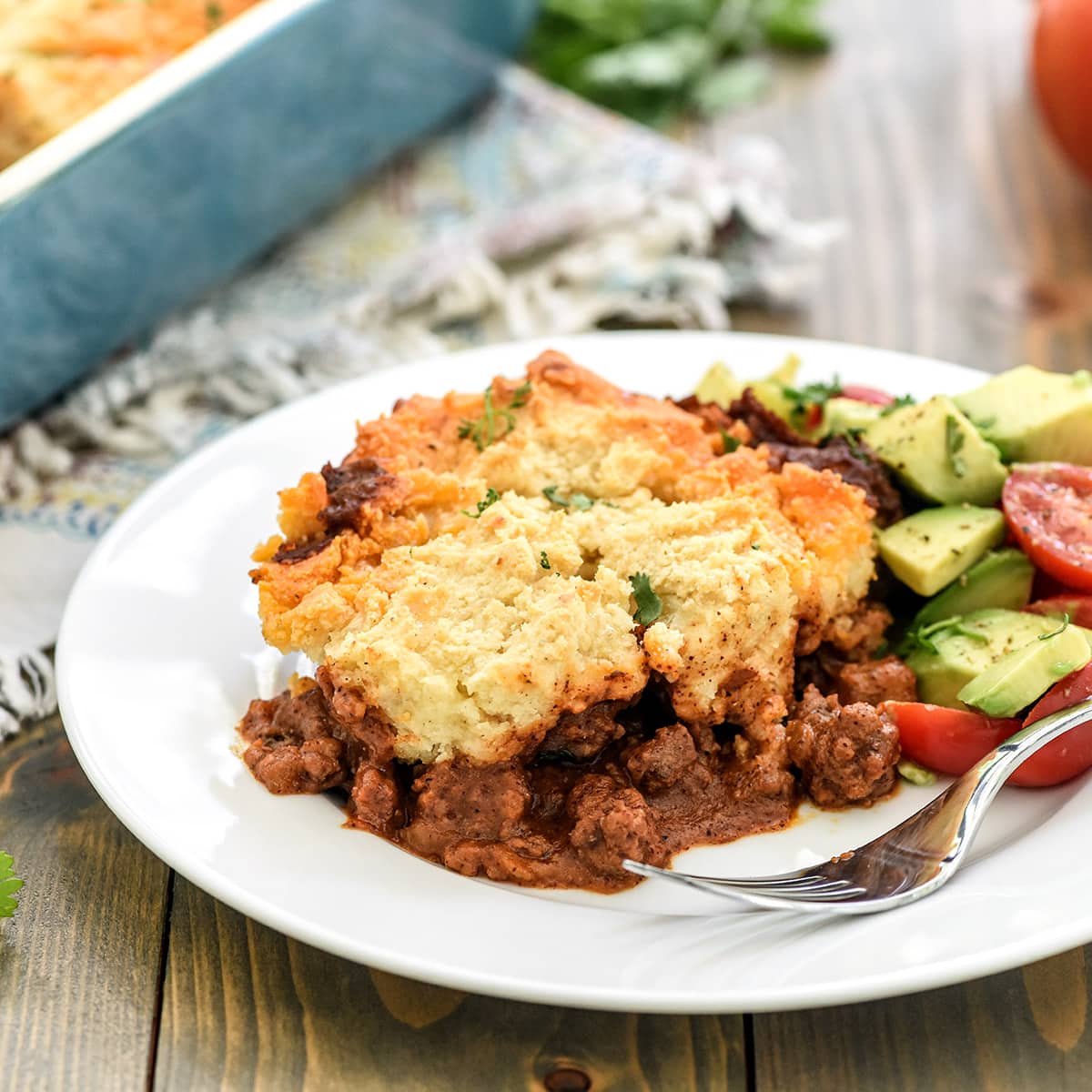Tamale Pie recipe served on a plate with avocado tomato salad on the side.