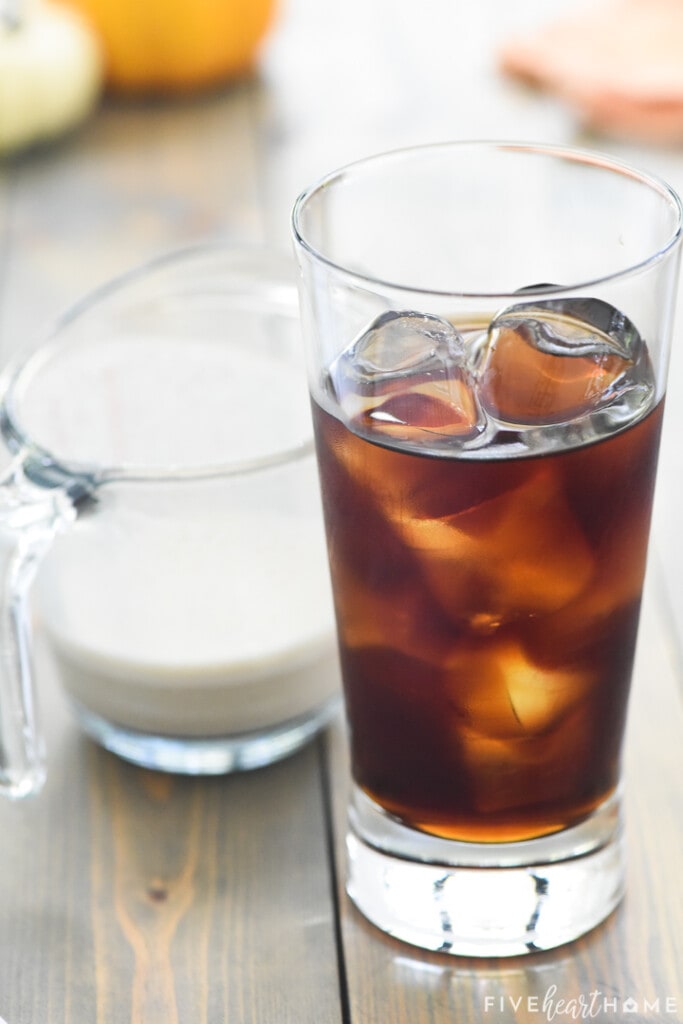 Glass of iced coffee next to measuring cup of foam for Pumpkin Cream Cold Brew recipe.