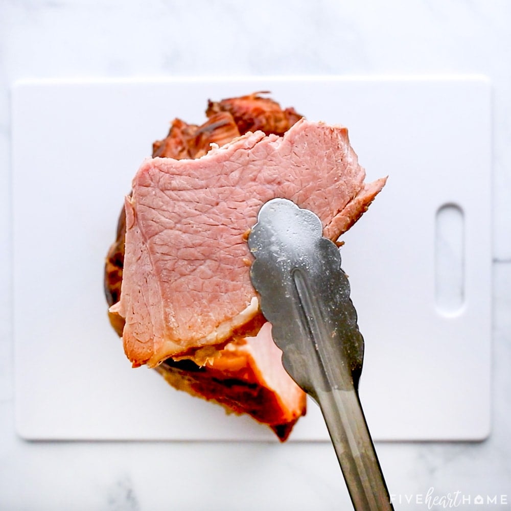 Crockpot Ham slices held by tongs.