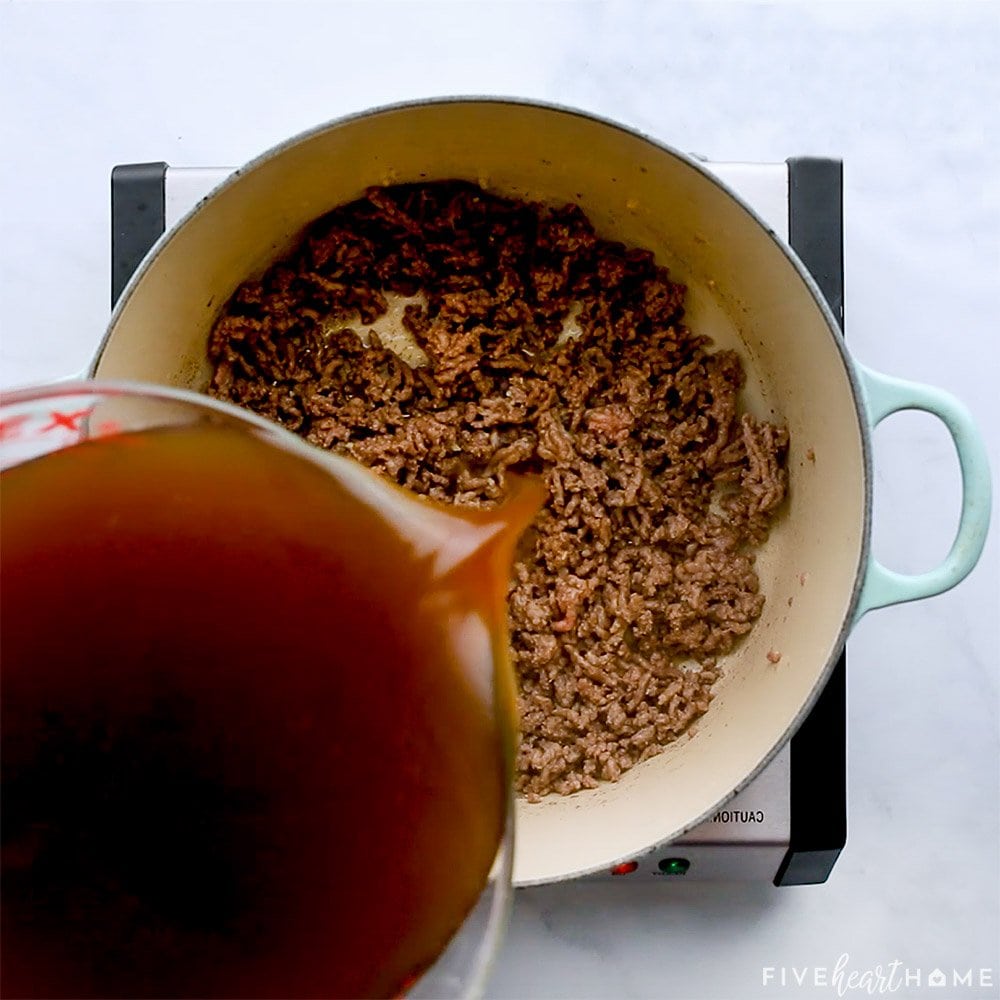 Beef broth being poured over ground beef.