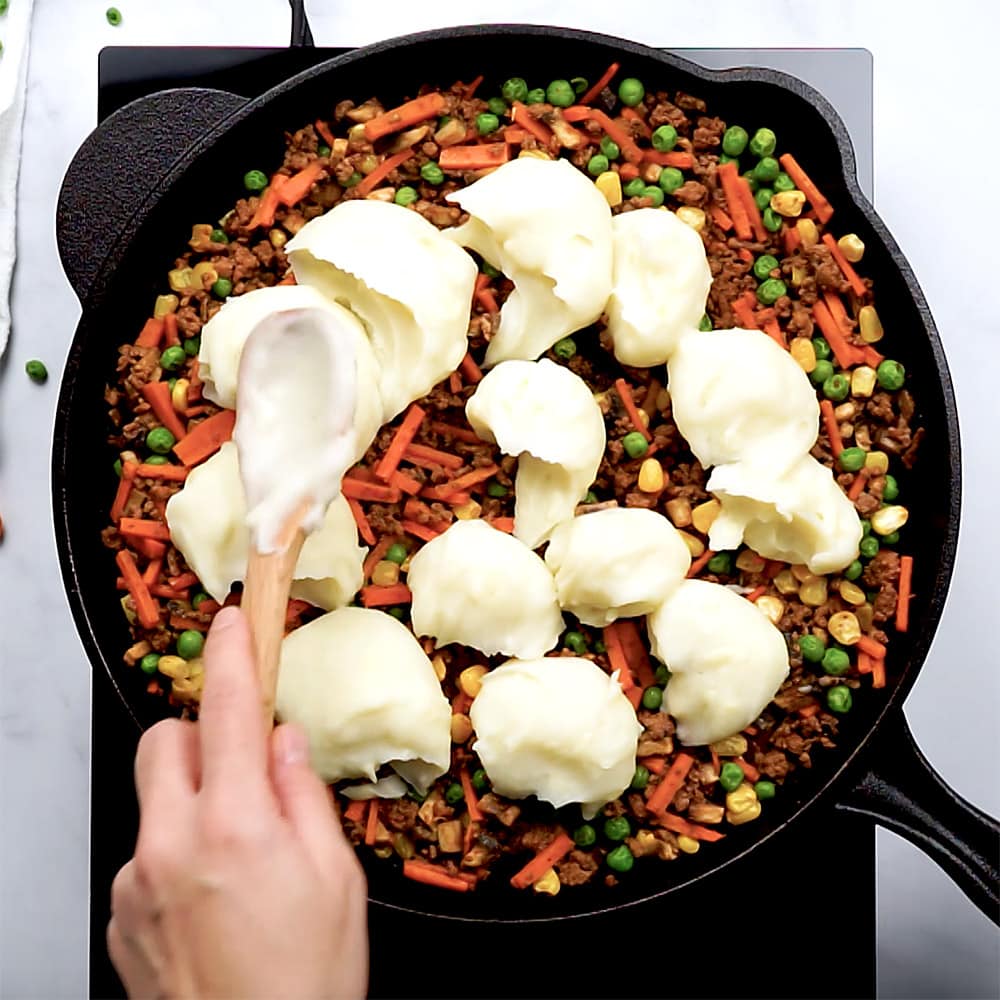 Dolloping mashed potatoes over Shepherd's Pie filling in skillet.