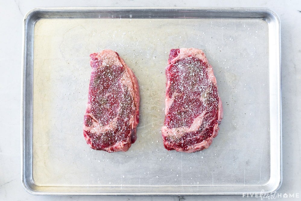 Aerial view of seasoned ribeyes on sheet pan.