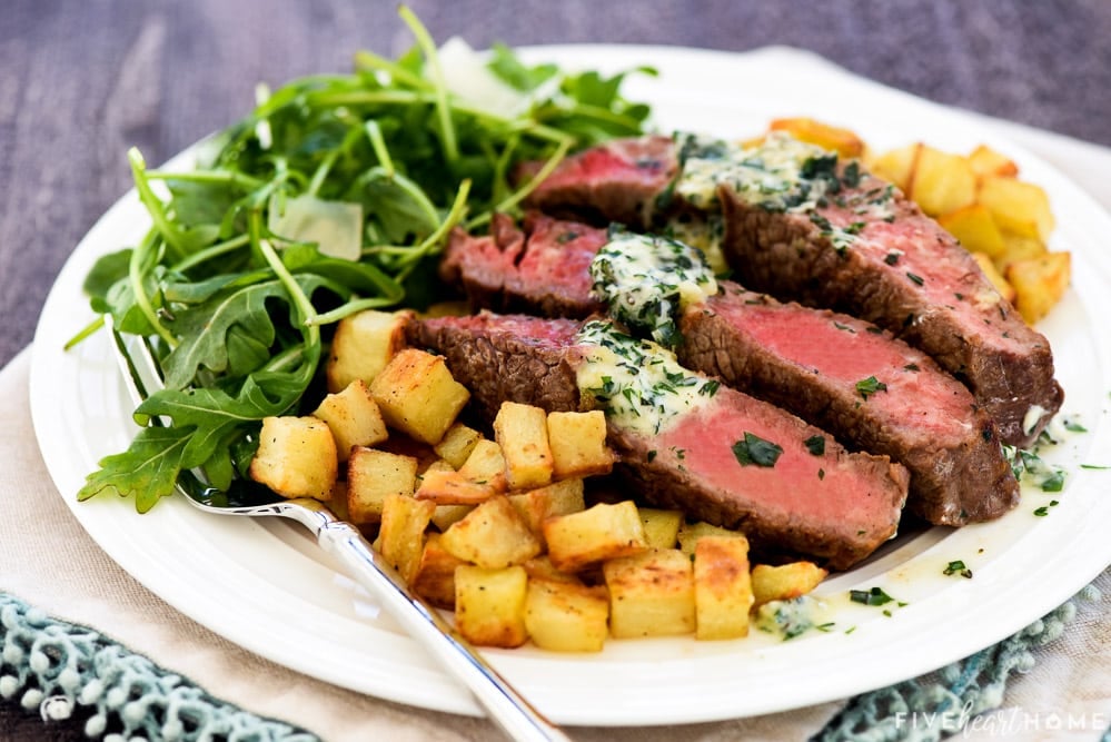 Plate of Steak Frites with sliced ribeye ararnged over roasted potatoes.