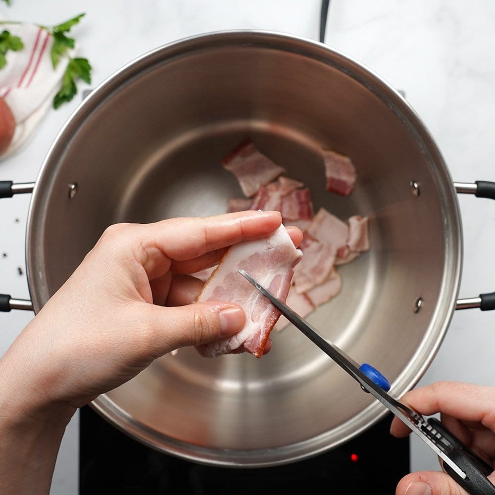 Snipping raw bacon into pot.