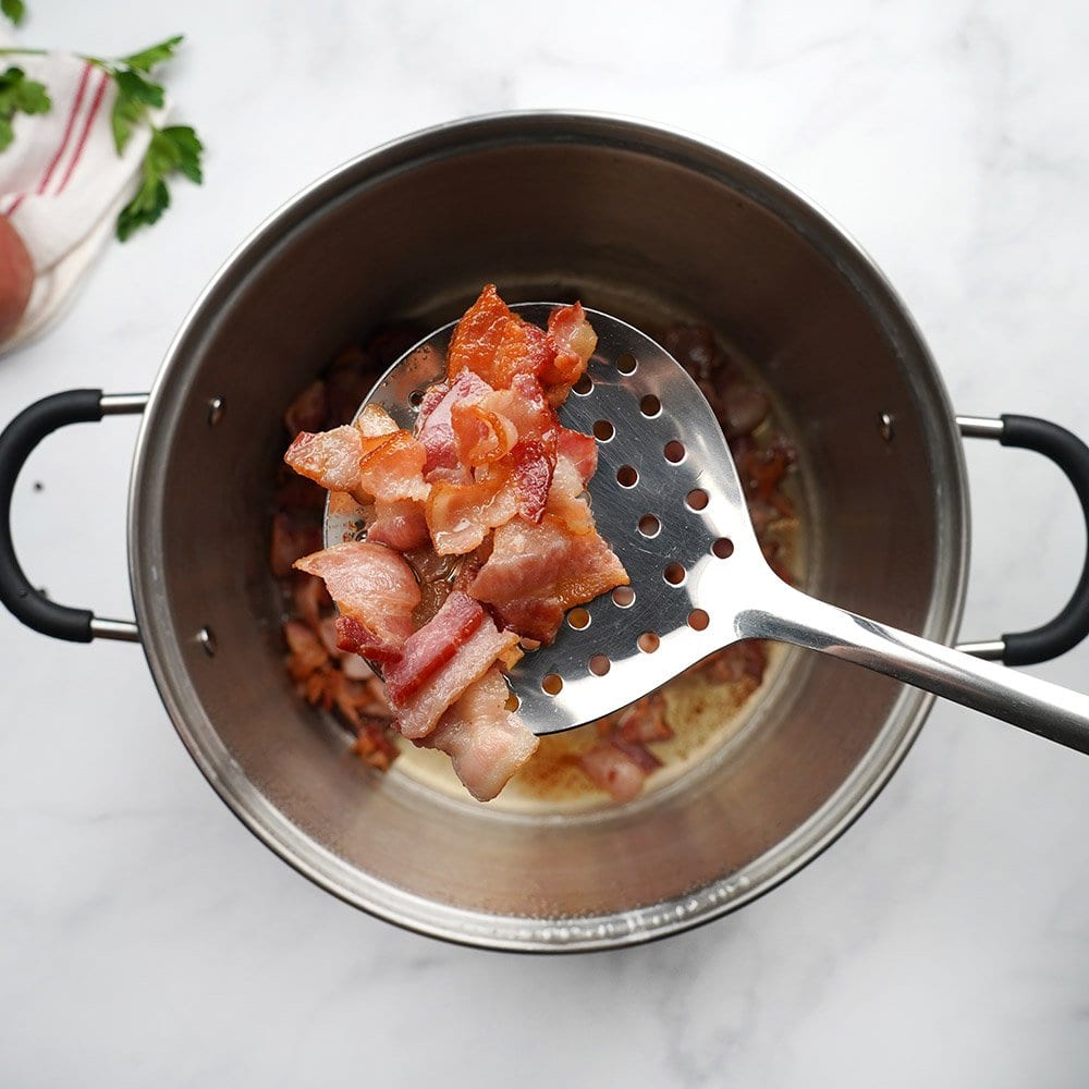 Cooked diced bacon on slotted spoon over pot.
