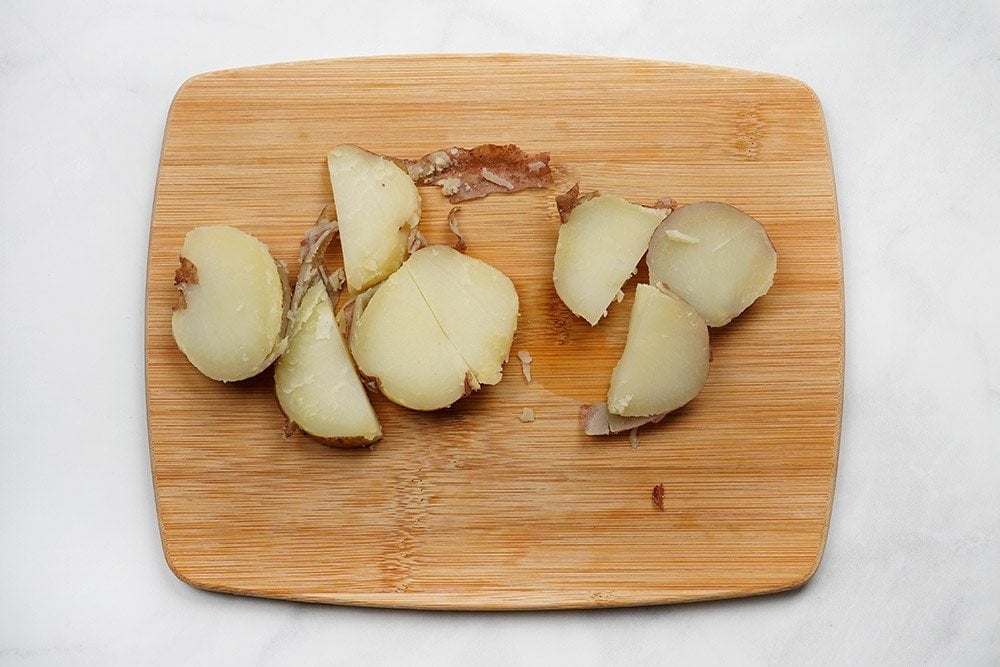 Slicing boiled potatoes on cutting board.