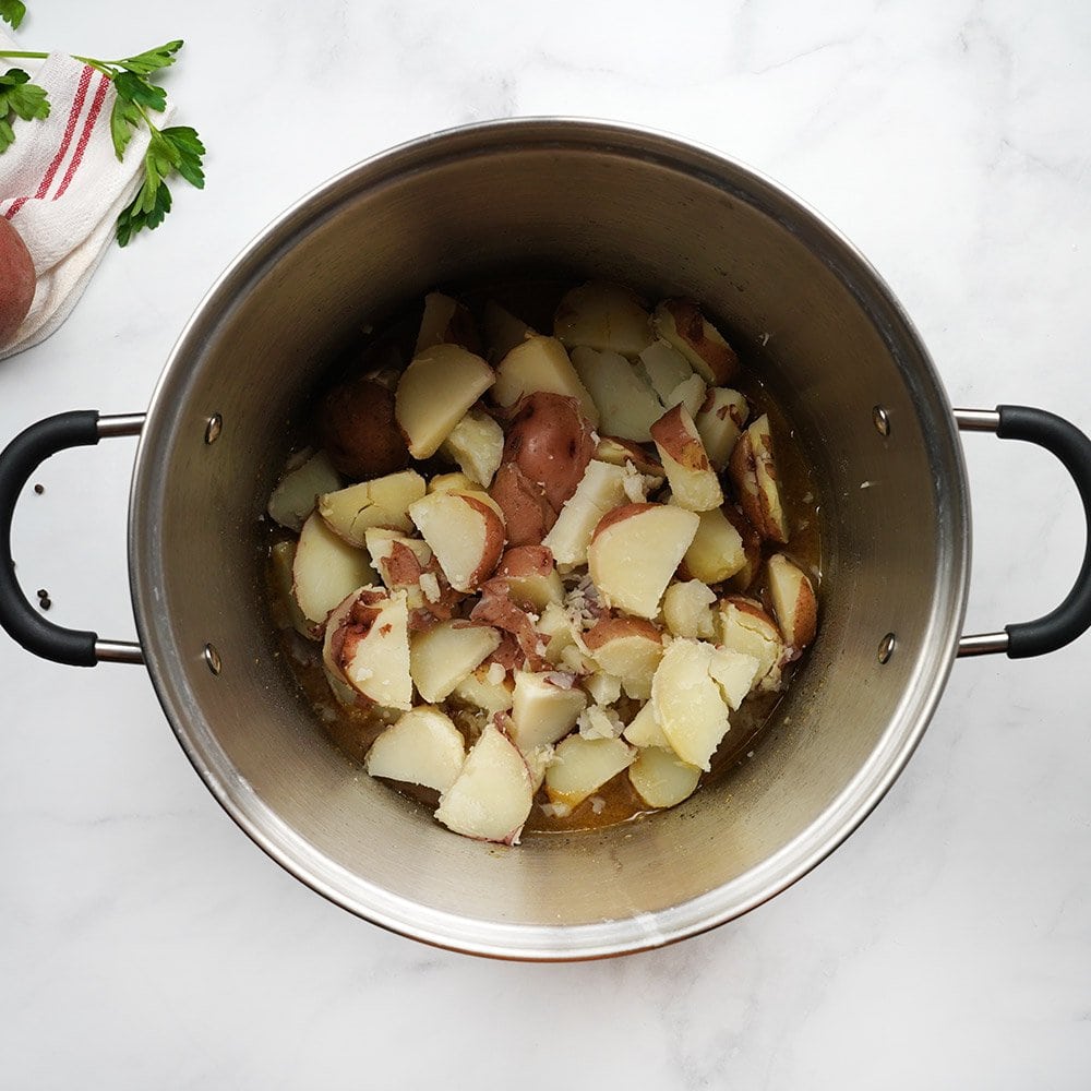 Adding sliced potatoes to pot of warm bacon vinegar dressing.