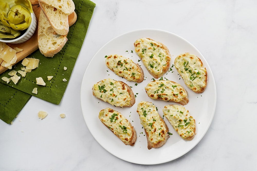 Aerial view of garnished Artichoke Bruschetta recipe on platter.