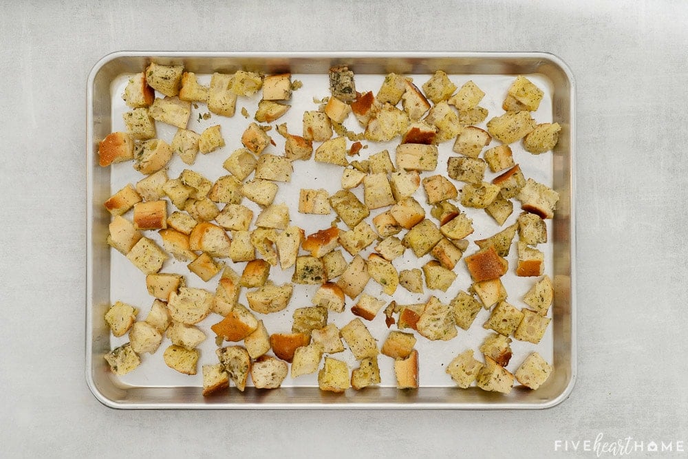 Cubes of bread with oil and hebs on baking sheet.