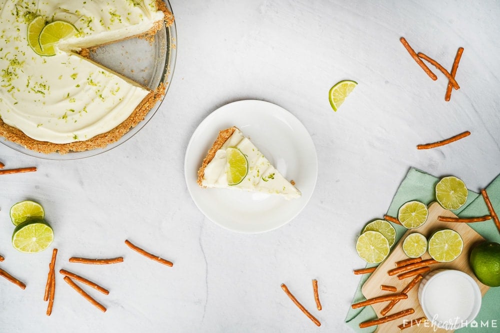 Aerial view of Frozen Margarita Pie in pan, on plate, an d with pretzels and limes scattered around.