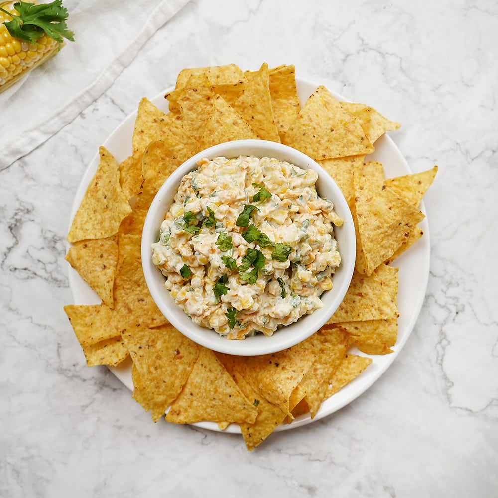 Aerial view of garnished Corn Dip recipe surrounded by tortilla chips.