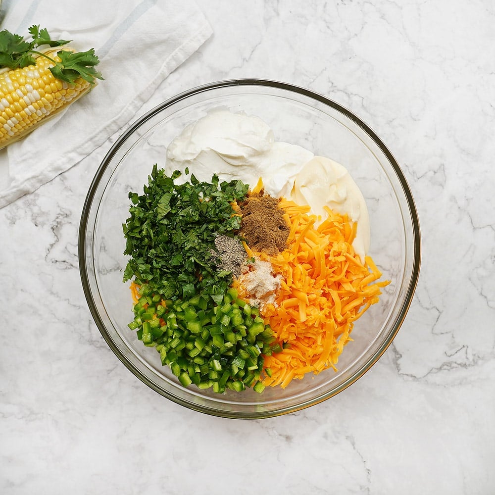 Aerial view of Corn Dip recipe ingredients in bowl, with fresh corn underneath.
