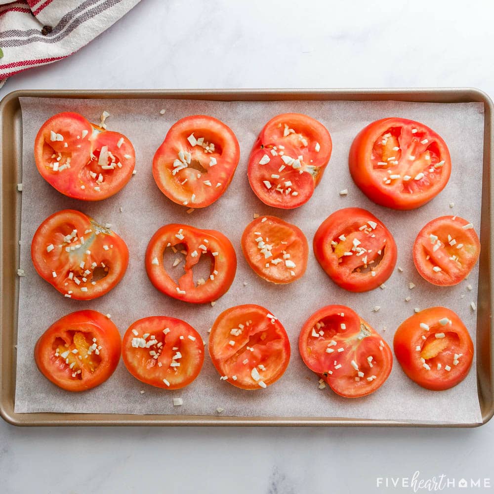 Tomatoes slices arranged on sheet pan and sprinkled with garlic.
