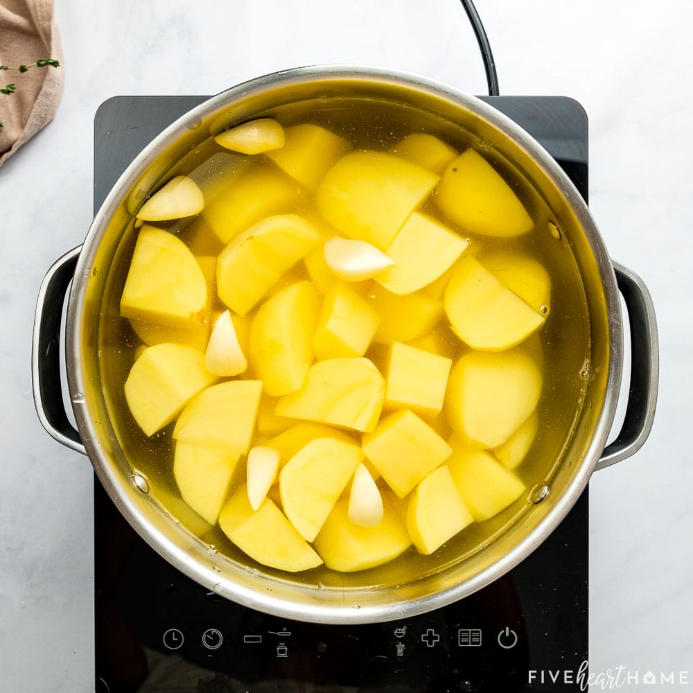 Potatoes and garlic cloves in pot covered with water.